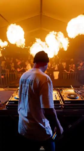MARK TARRO from behind at the DJ booth in front of an audience and flame effects
